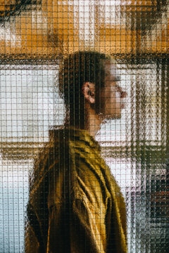 A man stands behind textured glass creating a surreal pixel pattern