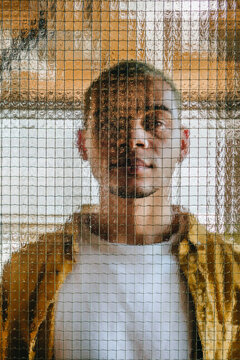 Portrait of a man looking through textured wire mesh glass