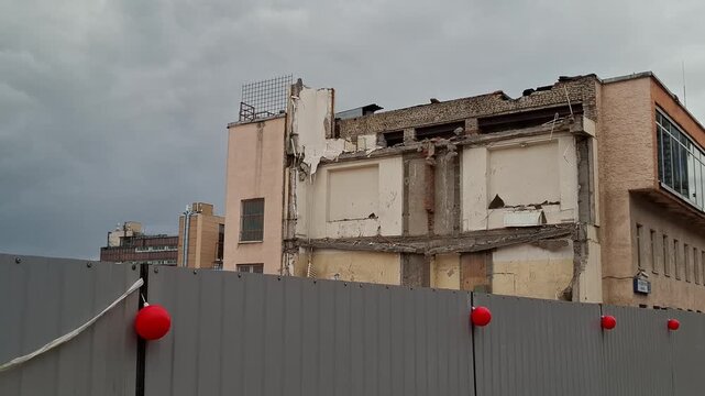 Old building demolition process behind a gray construction fence under a cloudy sky. urban renewal, city development, building construction.