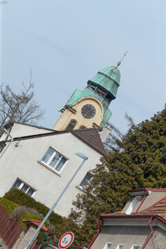 A copper-green domed church tower with a clock rises above pitched-roof suburban homes and evergreen trees. The composition is captured at an angle, showing