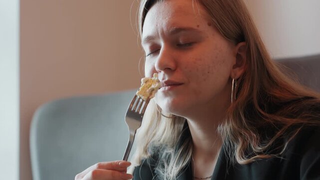 Young white woman savoring pasta on fork, cozy living room scene, content smile and soft warm lighting, freckled skin and hoop earrings, home chef and food blogger testing new recipe with gentle,