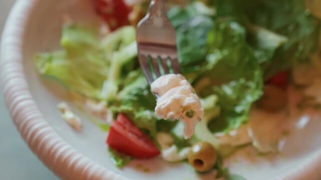 Fork scooping fresh salad with tomato and olive from paper plate, bright midday cafe lighting highlights crunchy romaine and tossed dressing, casual urban lunch scene with quick lifestyle bite