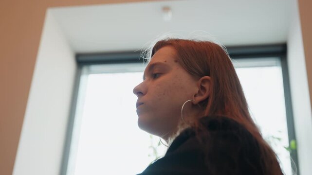 Young caucasian woman eating near window backlit silhouette subtle hand gesture lingering bite and thoughtful expression hoop earrings long hair soft overcast light intimate indoor dining scene