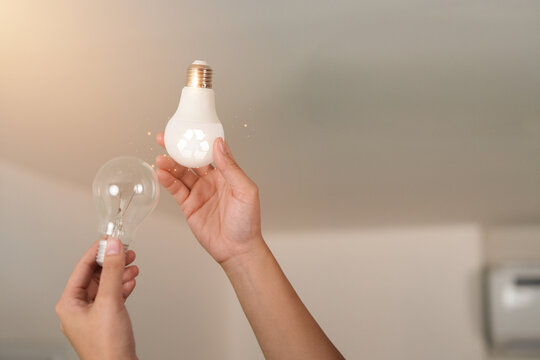 Hands changing incandescent bulb to energy efficient LED light bulb for power saving concept