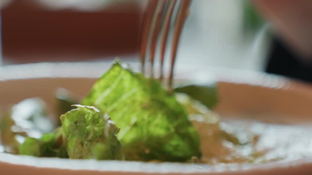 Fork lifting lettuce from ceramic bowl with glossy dressing, tines piercing romaine leaf, shallow focus and soft bokeh background, restaurant table setting, elegant dining ambiance, savoring bite
