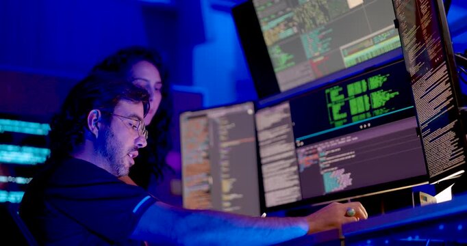Adult male cybersecurity analyst uses mouse while female colleague points toward code monitor, collaborating on digital system review, network security monitoring, and secure information analysis.