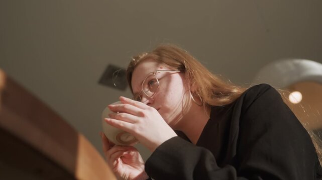 White woman inspecting tea cup closeup, lowangle indoor shot in warm cafe, glasses catching light, hands turning porcelain cup, concentrated expression studying color and aroma, rituallike tasting