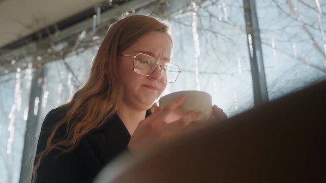 White woman in sunlit cafe checking smartphone, glasses reflecting window icicles, contemplative expression, warm backlight, subtle bokeh, modern interior, scrolling messages and planning work