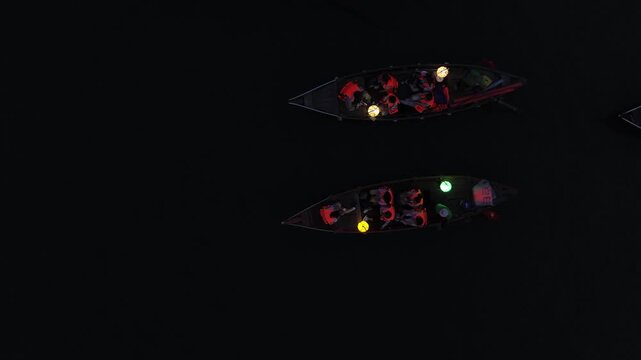 Aerial top-down view of people in two canoes with colorful lanterns floating on dark water