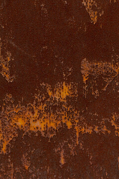 Close-up of a corroded metal panel with brown rust and flaking orange paint revealing layered deterioration. Rough pitted surface, irregular peeling edges