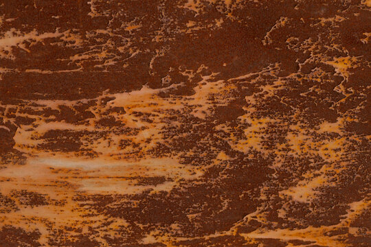 Close-up of an aged metal surface showing brown rust, flaking and peeling paint, and streaked corrosion patterns across the panel. Warm brown and ochre tones