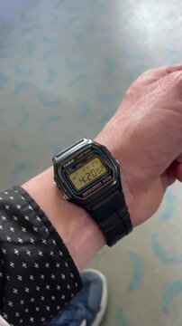 Wrist wearing digital watch shows time, commuter checking schedule in terminal carpet, sneaker and sleeve visible, hand gesture signaling hurry, casio