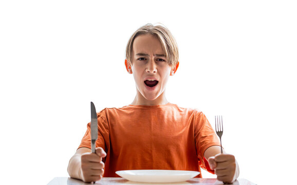 Upset little boy waiting for dinner while holding a fork, spoon. Hungry boy. Angry hungry boy child waiting for dinner. Holding fork and knife in his hands. Little boy sits in front of an empty plate.