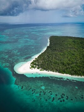 Aerial view of Balabac island featuring lush tropical forest, white sand beach, and turquoise waters with traditional outrigger boats in Balabac, Mimaropa, Philippines.