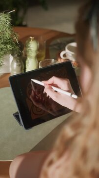 Creative artist illustrating flower pattern casually. Stylus used by artist creating botanical artwork peacefully. Relaxing artistic scene of drawing floral motifs amid cozy cafe surroundings