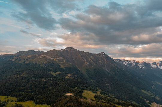 Aerial view of the Fiss region in the Tyrolean Alps, featuring lush green forests, mountain slopes, and a dramatic cloudy sky at sunset in Fiss, Tyrol, Austria.
