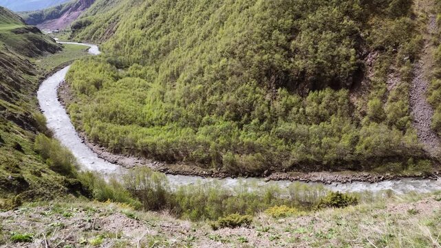 Aerial view of a mountain river winding through a lush green valley with snow capped peaks in the distance, perfect for travel, Truso valley, Georgia
