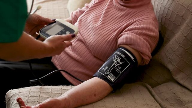 Nurse measuring blood pressure of elderly woman at home. Home healthcare visit, geriatric care, senior health monitoring, aging in place, medical assistance concept