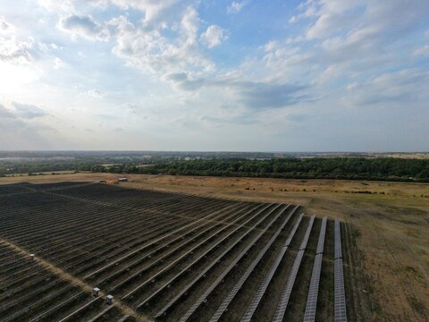 Aerial view of a large solar farm with rows of photovoltaic panels set in a rural landscape under a cloudy sky in Irchester, England, United Kingdom.