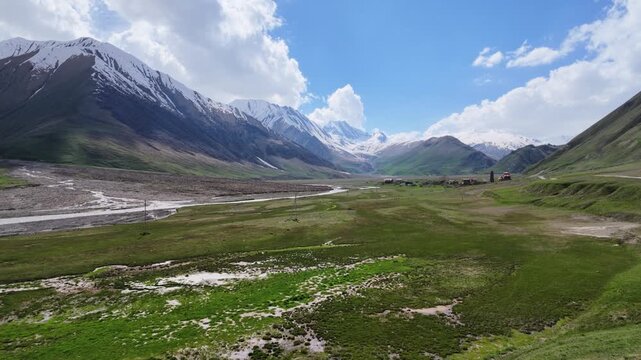 Panoramic view of majestic mountain range with snowy peaks, sprawling green valley, flowing river, traditional rural village houses, summer scenery, adventure travel, Truso valley, Georgia