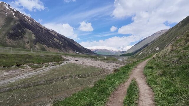 Panoramic view of a rugged Truso valley, Georgia with a winding dirt road and grassy hills, showcasing alpine landscape, hiking trails, wilderness adventure, and majestic nature scenery