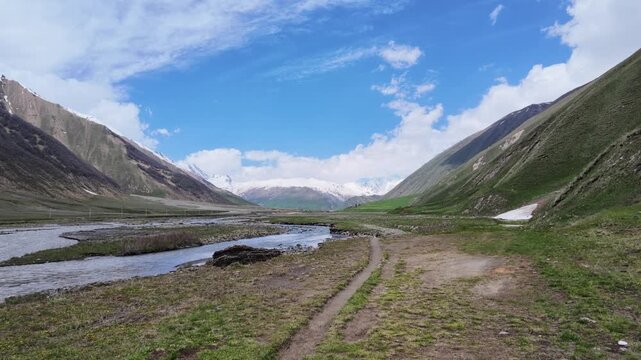 scenic mountain at Truso valley, Georgia with flowing river stream, melting snow peaks, lush green meadows, cloudy blue sky, perfect for travel, adventure, documentary background footage,