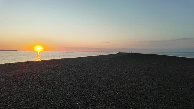 Colorful evening sunset on "The Street", a shingle ridge beach at Whitstable Beach, Kent, Southeast England, UK. 4K low angle reverse shot facing the vibrant colors of the horizon.