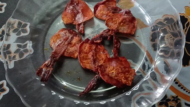 Roasted cuttlefish pieces served on a clear glass plate, featuring golden-brown crispy edges and grilled texture, a popular seafood dish enjoyed as a savory snack or meal.