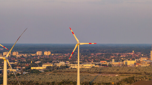 Aerial view of wind turbines standing in a field with a town in the background under a soft sky in Level, Hungary.