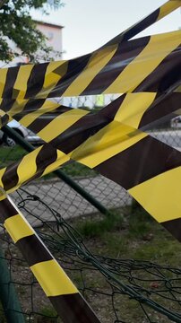 Passerby walking behind yellow black tape near fence, urban pedestrian moves past apartment blocks and parked cars, ribbon fluttering in evening