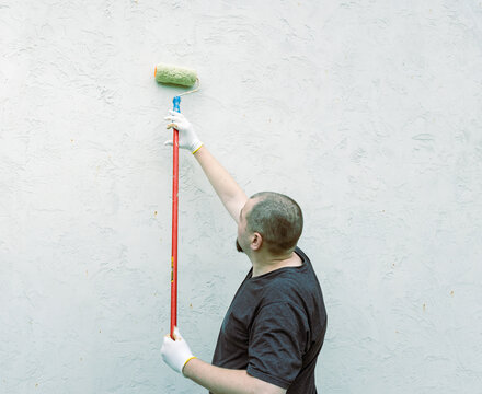 Man paints wall with roller, wearing gloves