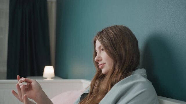 Caucasian teen laughing while filing nails, wrapped in blanket beside soft lamp, candid smile, cozy bedroom vibe, youthful downtime and gentle selfcare, lighthearted pamper moment, student break mood