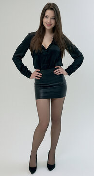 Junge br&uuml;nette Frau im schwarzen Minirock, Blazer und High Heels posiert selbstbewusst vor neutralem Hintergrund. Elegantes Fashion-Portr&auml;t, Business-Look und moderner Glamour.