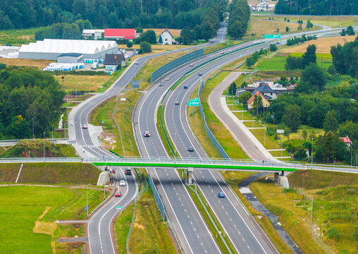 Aerial view of the Droga Ekspresowa S6 expressway with a green bridge crossing over the highway, surrounded by lush fields and trees in Slupsk, Pomeranian Voivodeship, Poland.