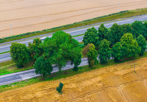 Aerial view of Droga Ekspresowa S6 expressway winding through golden wheat fields and lush green trees in Slupsk, Pomeranian Voivodeship, Poland.