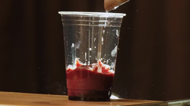 Barista drops ice into clear plastic cup with cherry base. Woman adds cubes from small scoop starting chilling red fruit layer for cafe drink