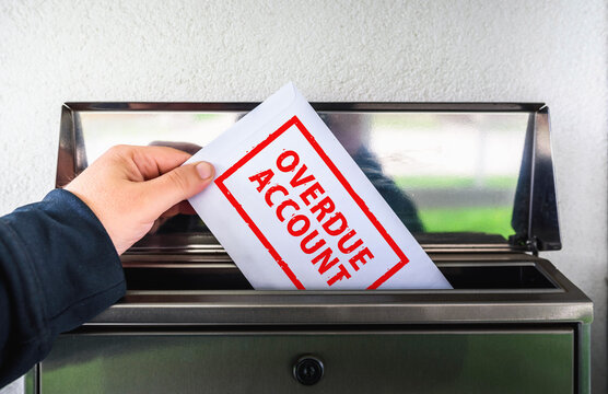 Hand Inserting Envelope with "Overdue Account" Text into Mailbox. A visual concept representing unpaid bills, debt collection, financial stress, and late payment notices.