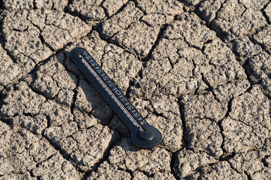 Analog thermometer showing extreme heat on cracked dry soil, illustrating drought, global warming, climate change, heatwave, water scarcity and environmental crisis with copy space.