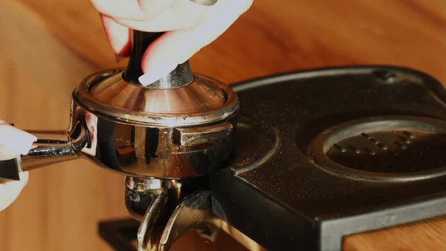 Barista hands press ground coffee in stainless portafilter at countertop closeup. Delicious strong caffeine drink preparation process in coffeeshop