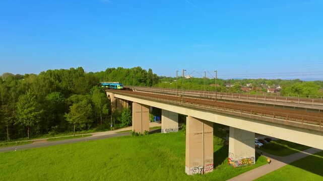 Regionalzug f&auml;hrt &uuml;ber eine Br&uuml;cke. Blauer Zug f&auml;hrt vor blauem Himmel und gr&uuml;nen B&auml;umen. Westfalenbahn f&auml;hrt ein.