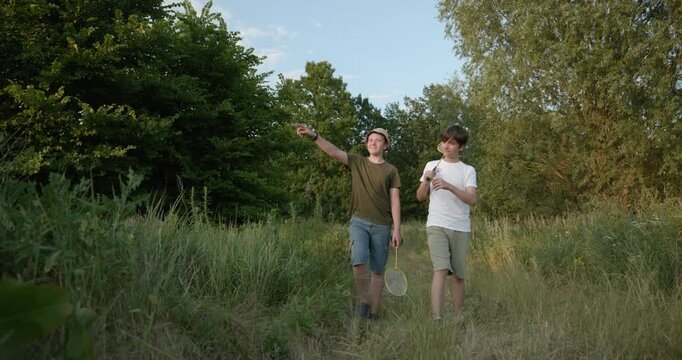 Two boys play badminton on nature. Teenagers spending time together. 4K 10-bit