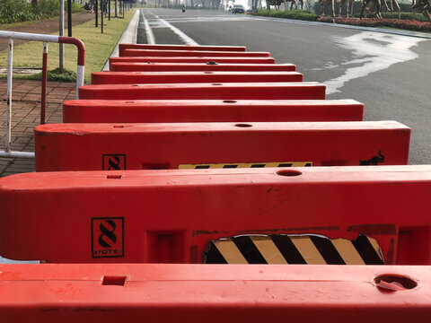 Close view of red plastic barricades aligned beside wet asphalt, ideal for lane closure, construction safety, traffic control, road maintenance, and urban infrastructure.