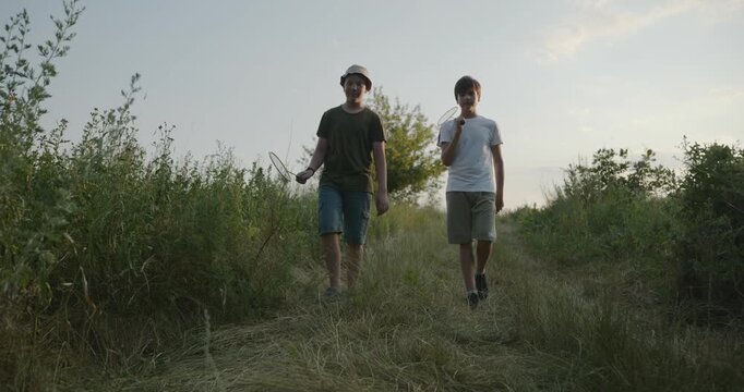 Two boys play badminton on nature. Teenagers spending time together. 4K 10-bit