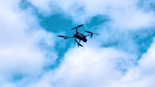 Drone flying against a vibrant blue sky with fluffy white clouds and dynamic angles captured