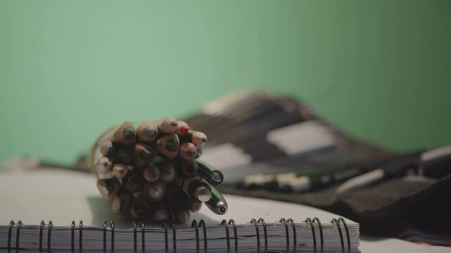 Colored pencil bundle placed on spiral sketchbook with artist tool kit on green screen background studio.