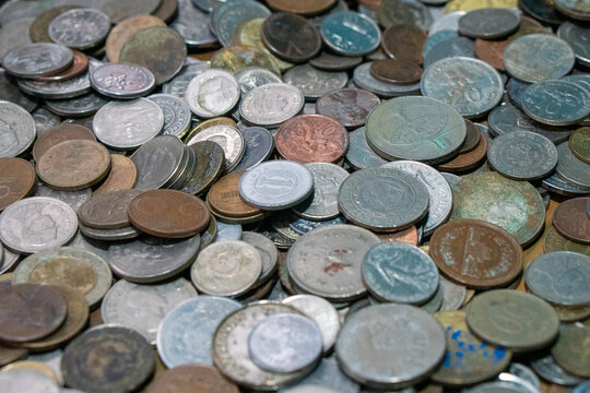 Large pile of assorted metal coins ranging from vintage pieces to those once in circulation from various countries spread across a flat surface. 