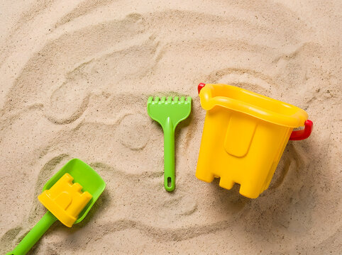 Bright Yellow Sand Bucket and Green Shovel Toy Set on Beach Sand | Childrens Beach Toys Sand Castle Bucket Rake and Shovel Top View | Summer Beach Sand Toys Laying Flat on Texture Sand Surface 