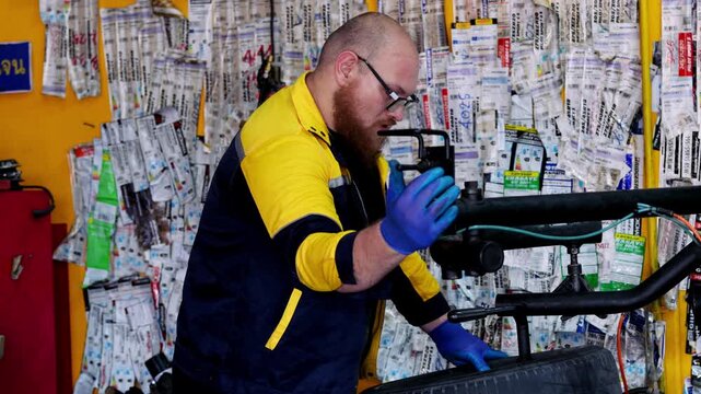 Skilled professional mechanic focused on repairing automotive tire wheel inside modern garage workshop with serious expression and diligent work ethic