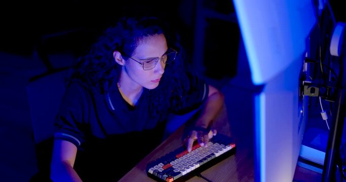 Adult female technology professional works at computer station, uses keyboard and reviews digital information on monitor during cybersecurity analysis and system monitoring in operations workplace.