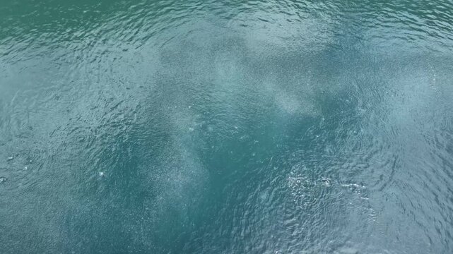 Clear turquoise water surface with gentle ripples and tiny bubbles rising, perfect for background texture, tranquil nature scene